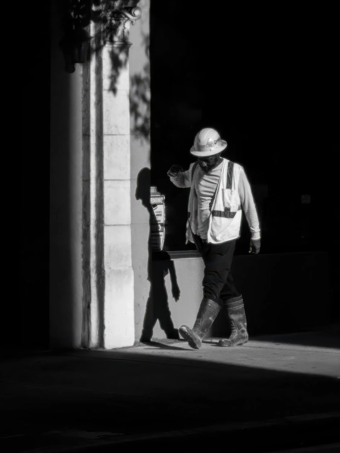 Black and white photograph of a construction worker in a hard hat stepping into a narrow beam of light between two dark walls in Miami