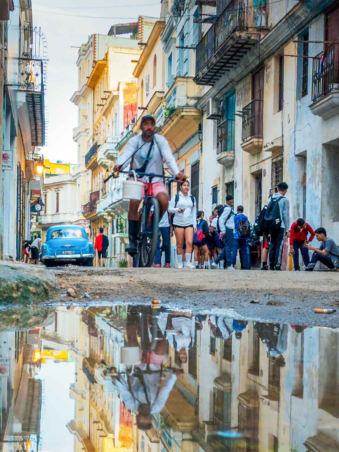 Old Havana Cuba street scene with locals walking past vibrant colonial architecture and vintage vehicles.