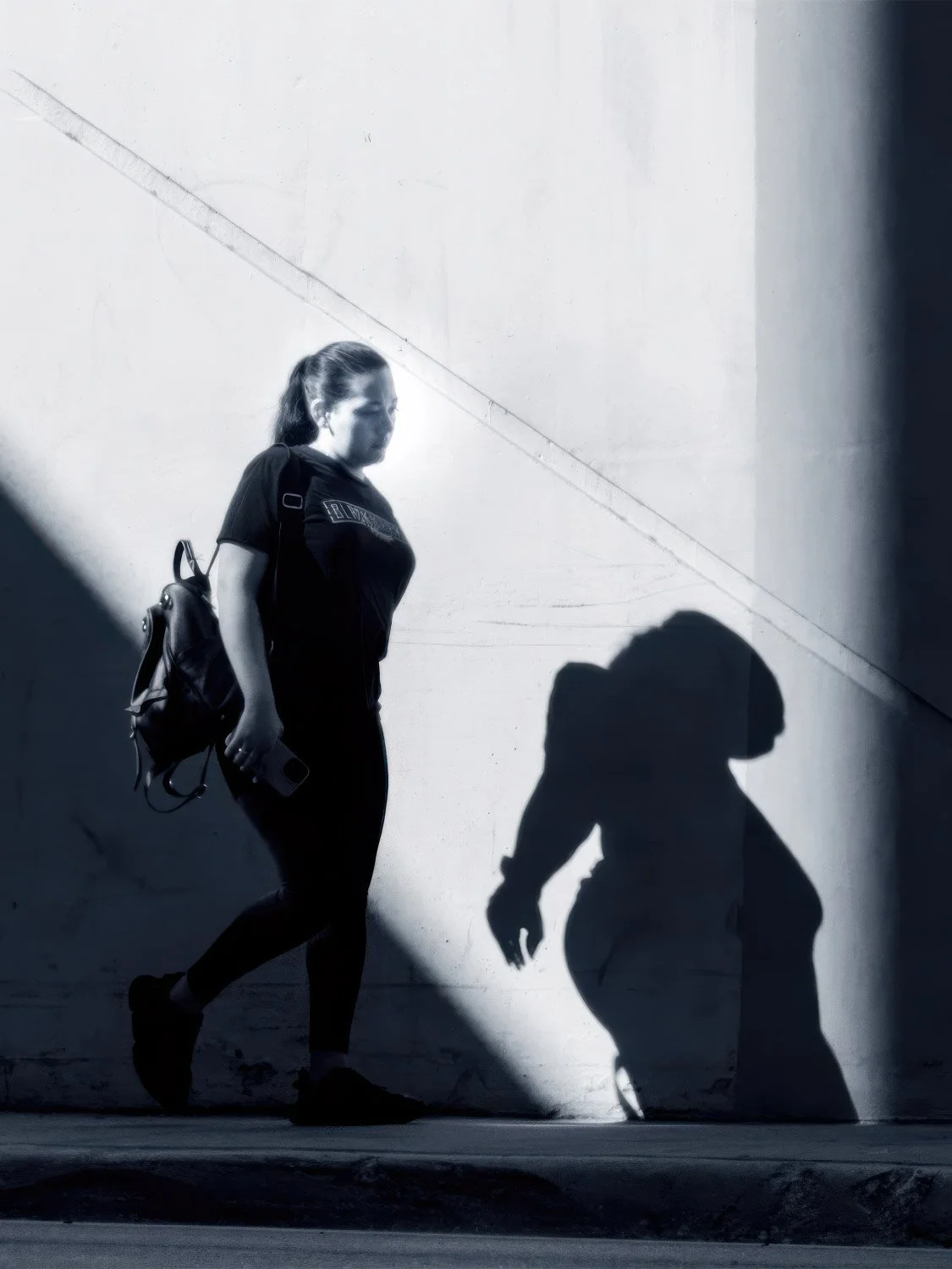 Woman walking with shadow Black and white street photo of a woman walking with a bold shadow cast on the wall behind her in Miami