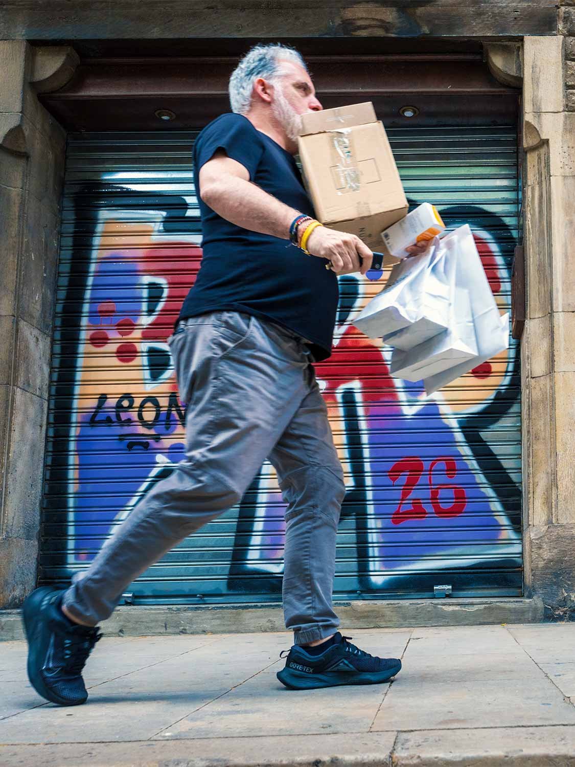 Man hurrying past a graffiti-covered shop shutter in the Gothic Quarter, carrying boxes and shopping bags