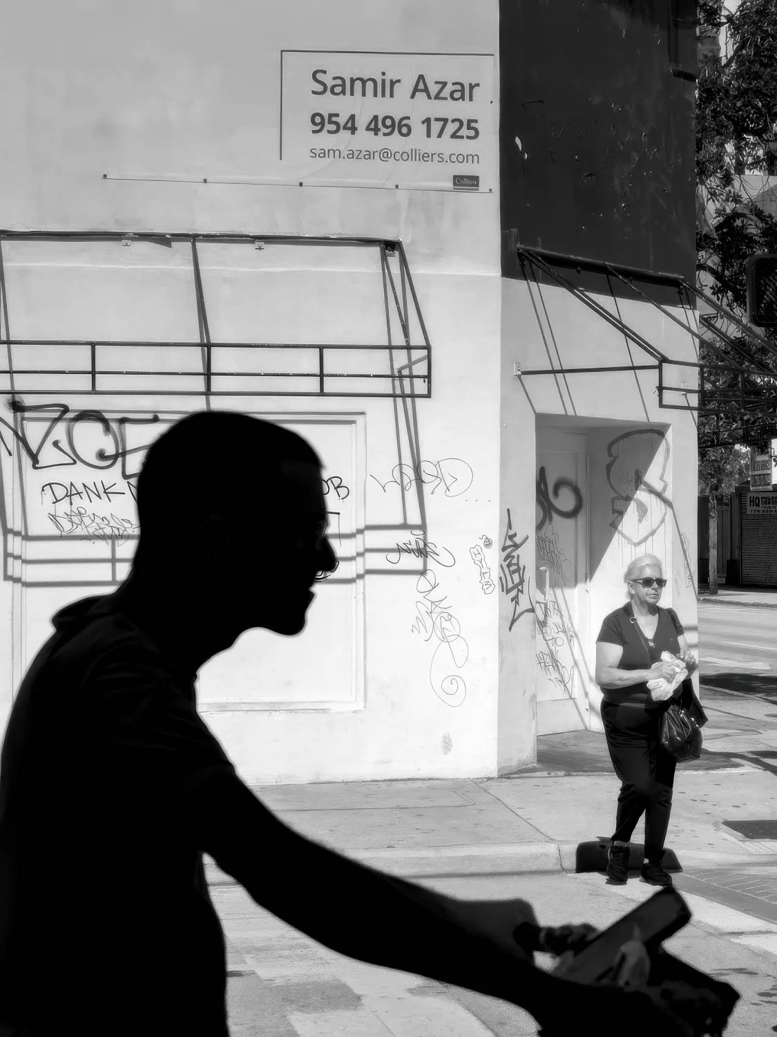 Cyclist silhouette & graffiti wall Black and white street photo of a cyclist silhouette in the foreground with a woman standing near a graffiti-covered wall in Miami