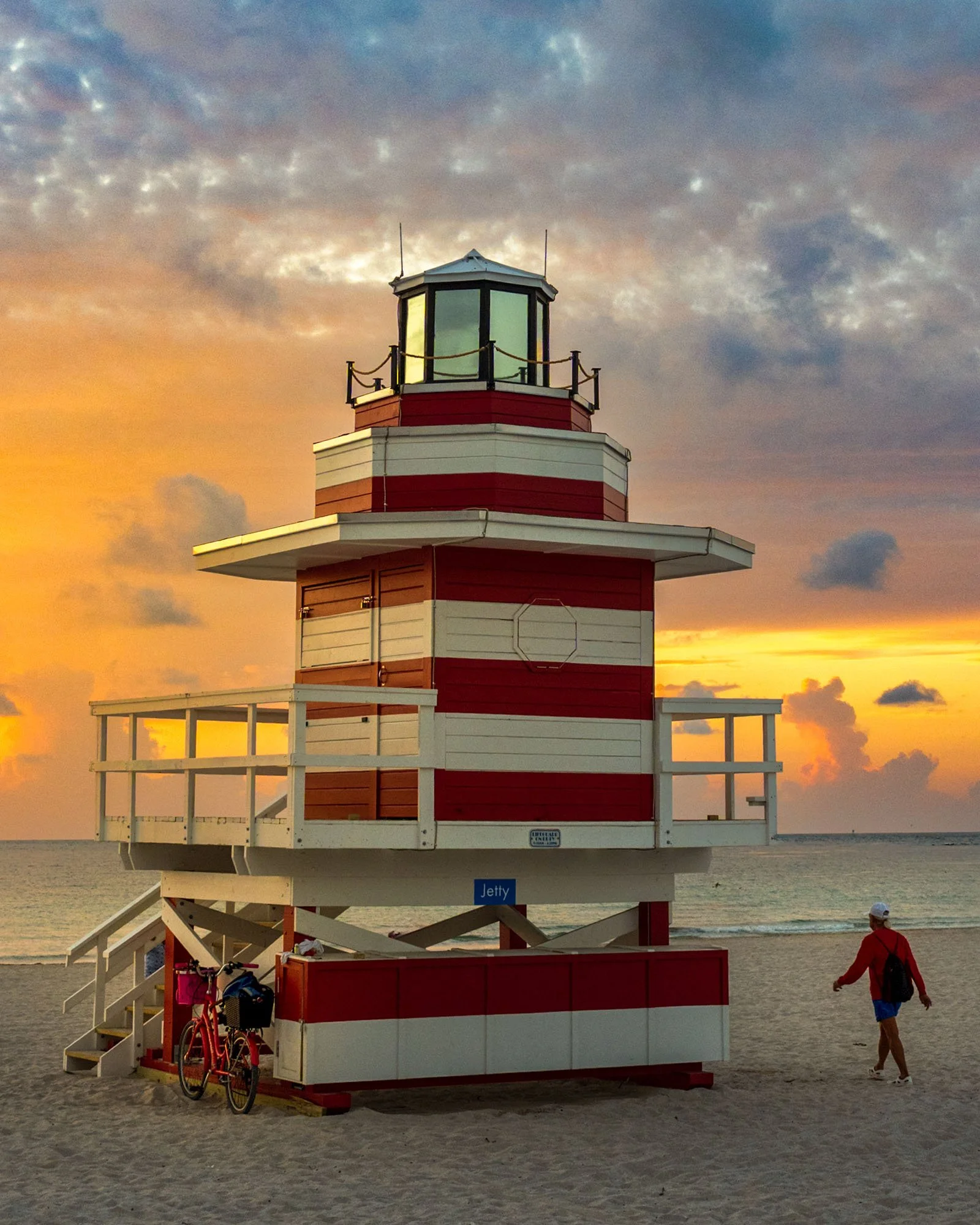 New Jetty lifeguard tower at sunrise on South Beach with a bicycle parked under the deck and a beachgoer walking by