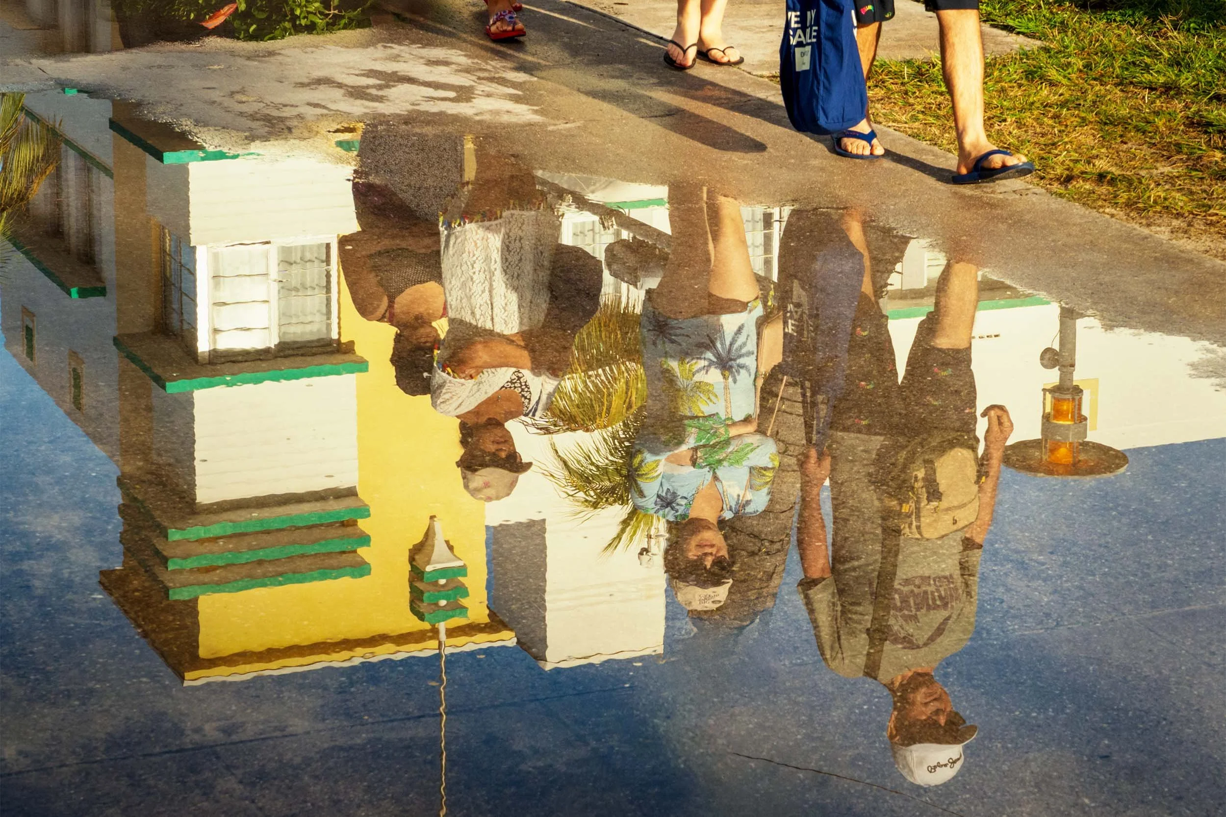 A group of tourists reflected in the water on the sidewalk while walking thru Lummus Park in South Beach Miami