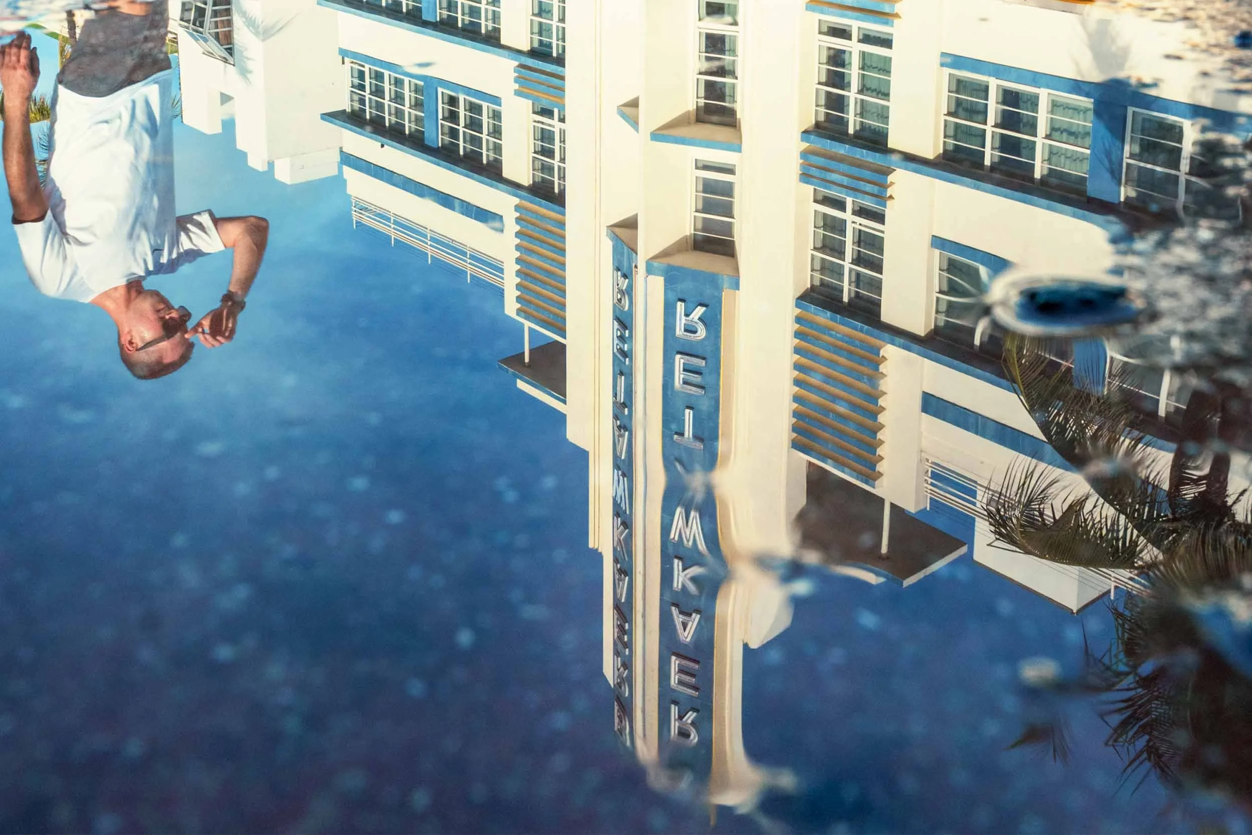 Photographer crouching low to capture a puddle reflection of Art Deco buildings on Ocean Drive, South Beach Miami