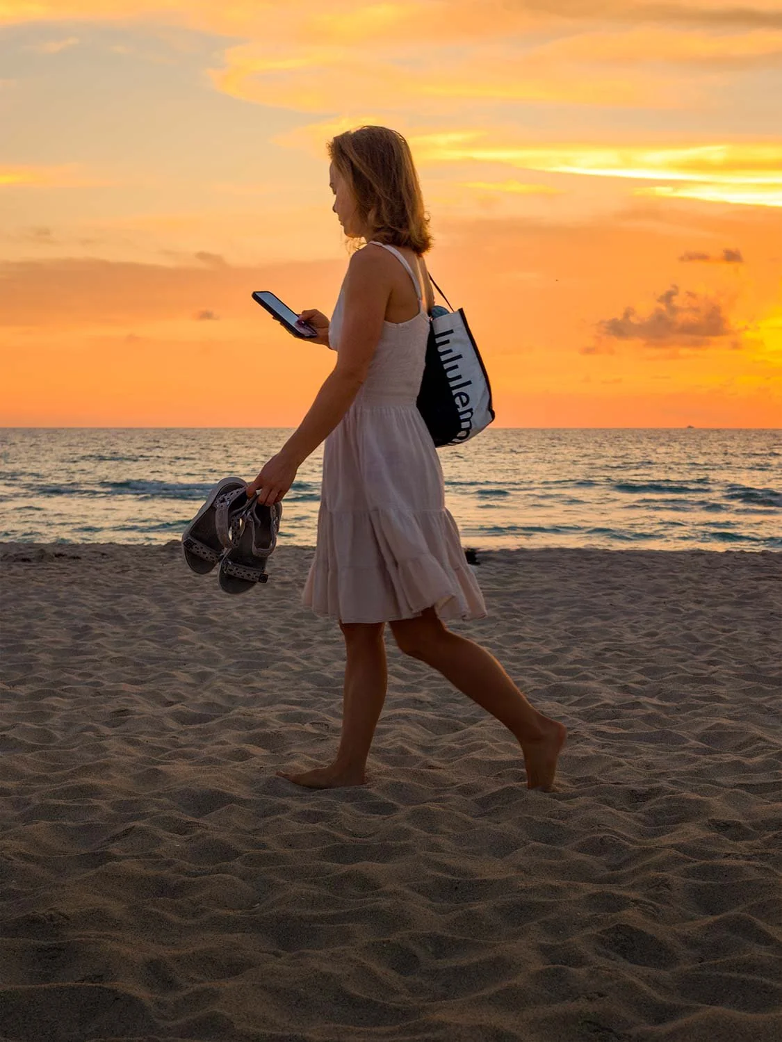 Woman walking barefoot along South Beach Miami at sunset carrying sandals