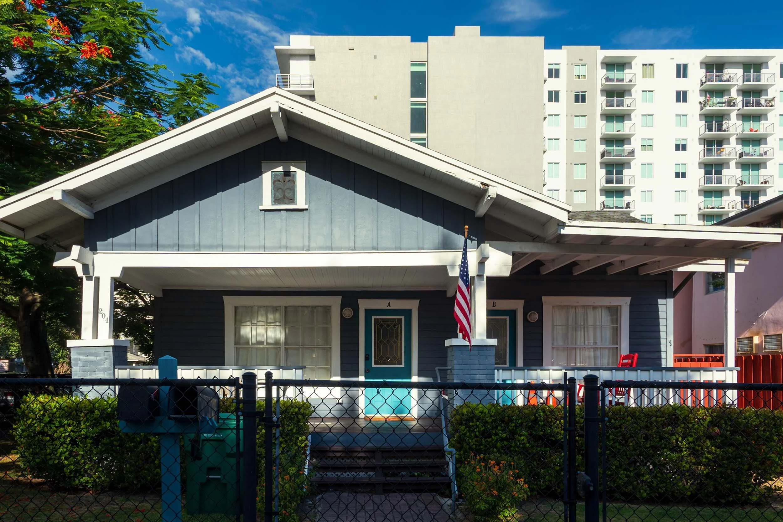Navy blue wood-frame duplex with an American flag, high-rise tower behind it, Miami