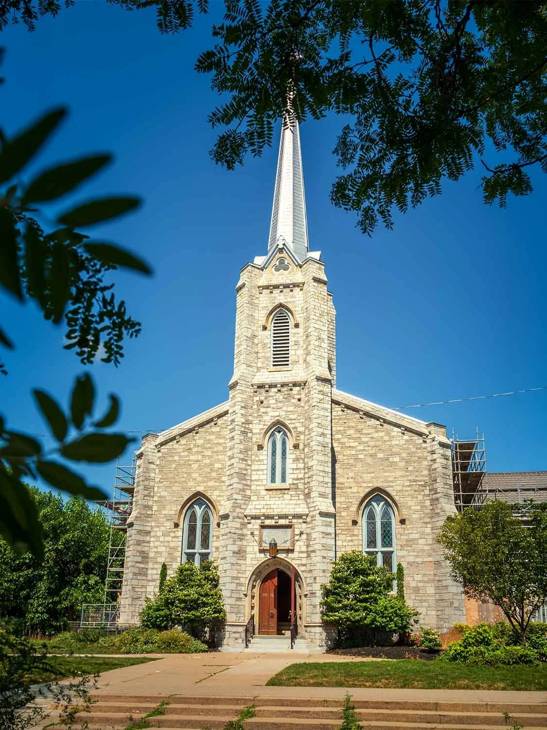 Gothic Revival stone church steeple historic landmark religious building architecture sunny blue sky scaffolding renovation