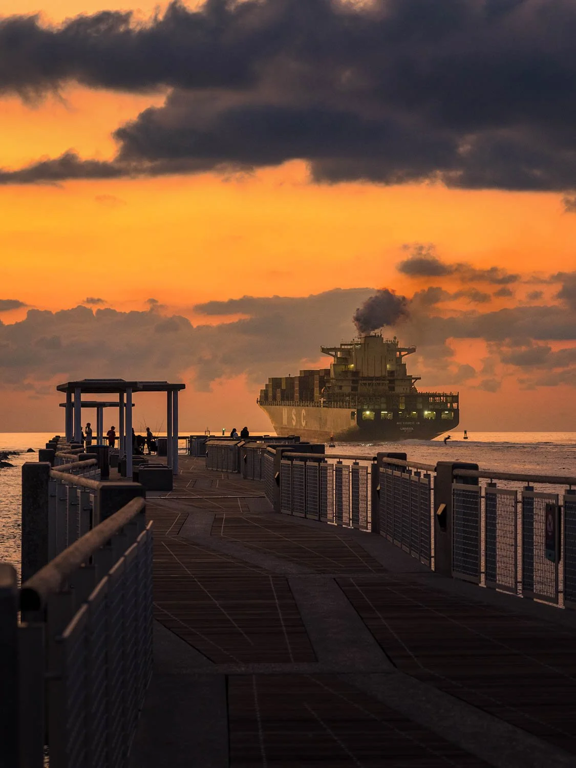 Cargo ship sailing past South Pointe Pier in South Beach as early morning light reflects across the ocean.