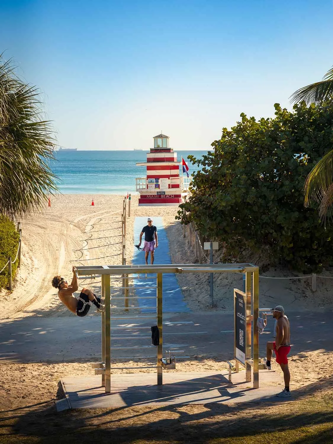 Men doing pull-ups along the boardwalk at South Pointe Park in South Beach Miami, with ocean and coastal scenery.