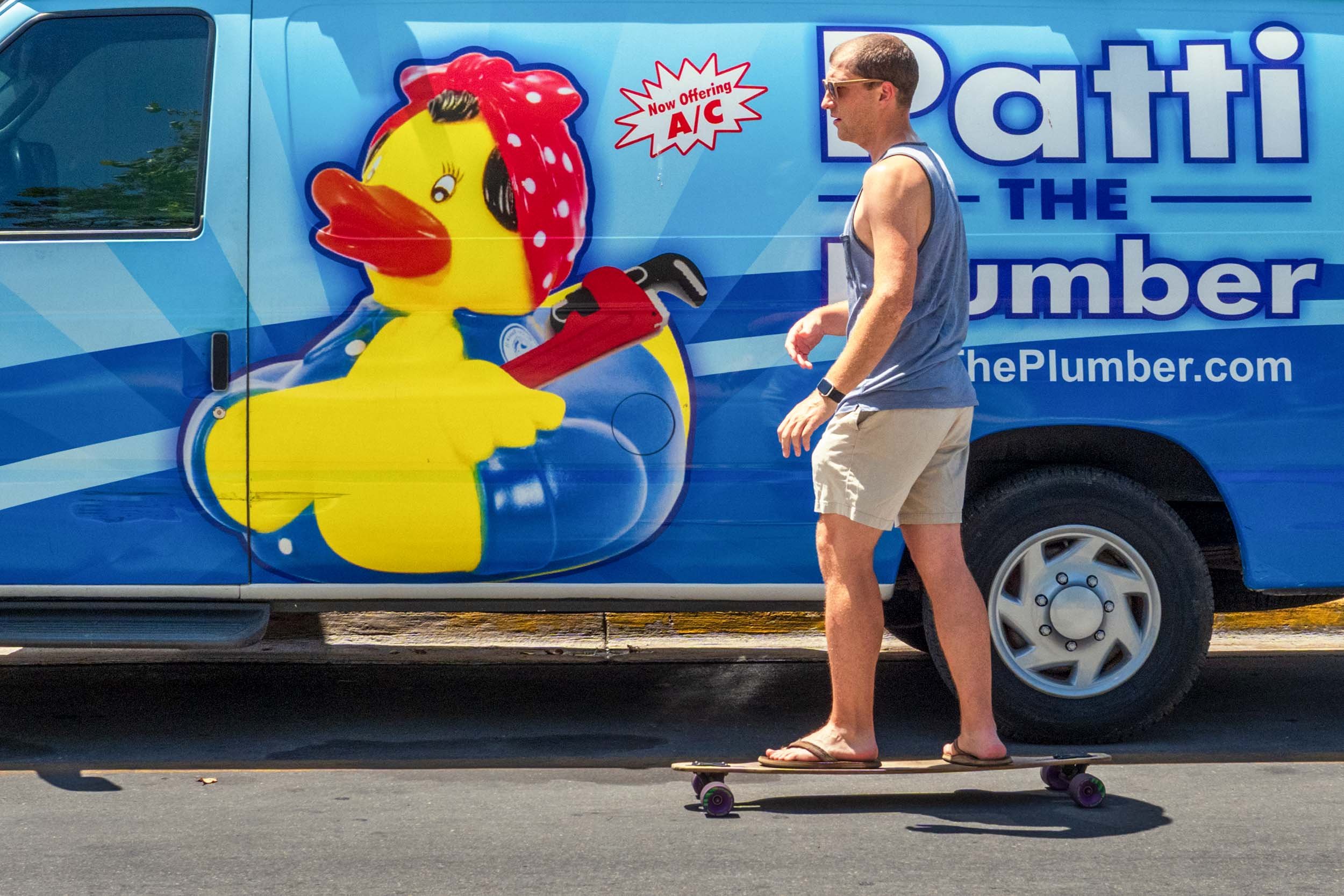 Man on longboard skateboard passes a blue Patti the Plumber service van in Key West, FL
