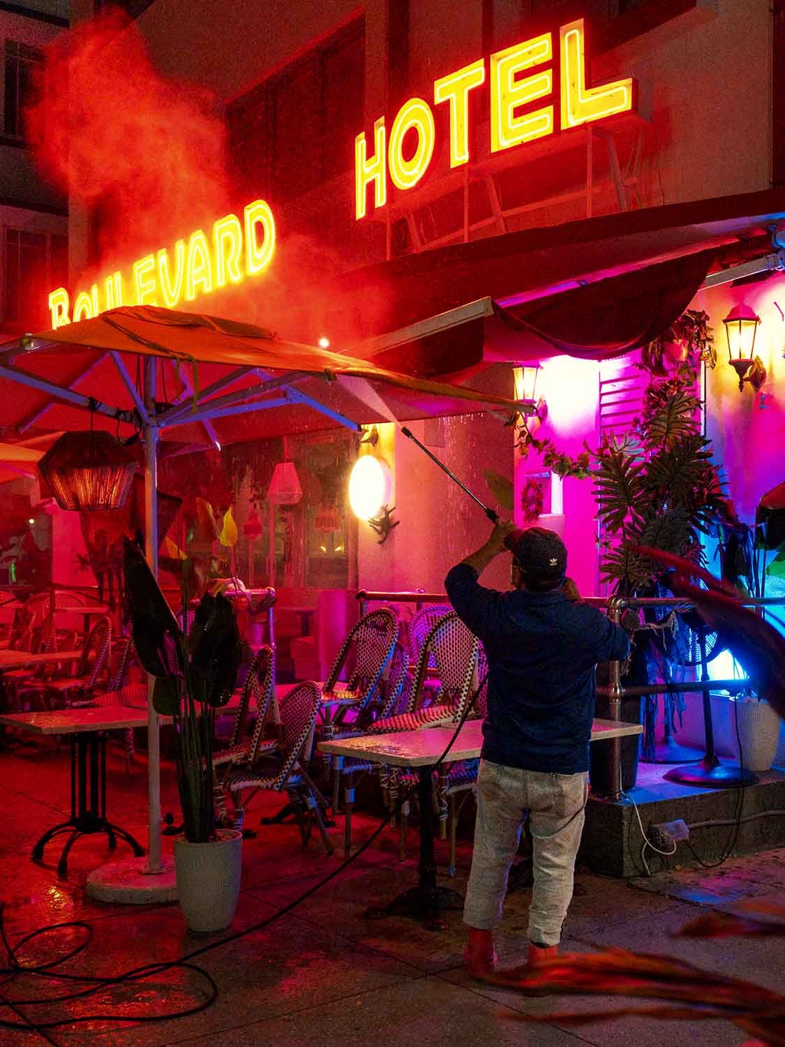 Worker pressure cleaning neon sign at the Boulevard Hotel on Ocean Drive in South Beach Miami before sunrise, with Art Deco architecture and early morning light.