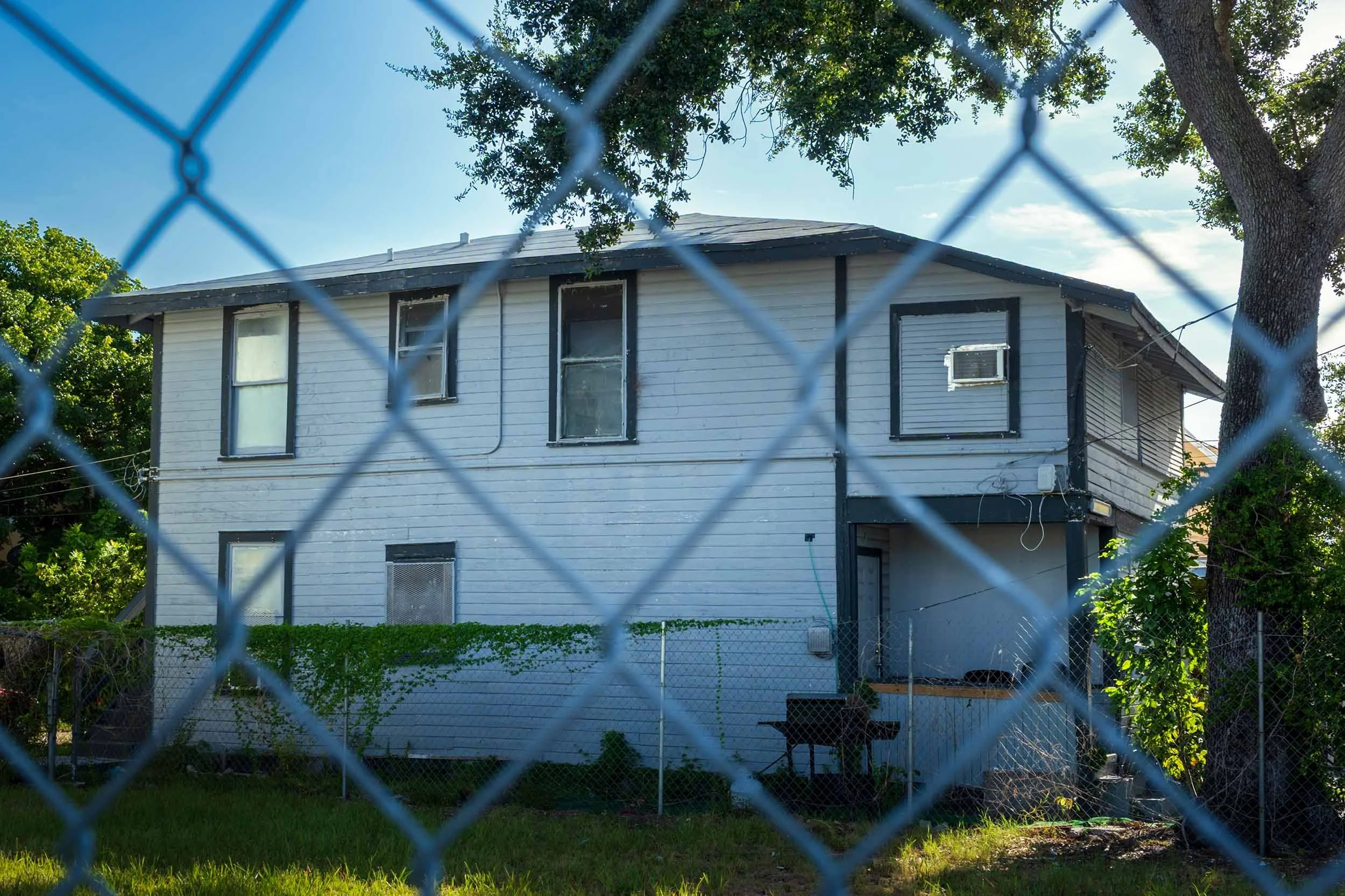 Two-story white wood-frame house behind a chain-link fence in Miami