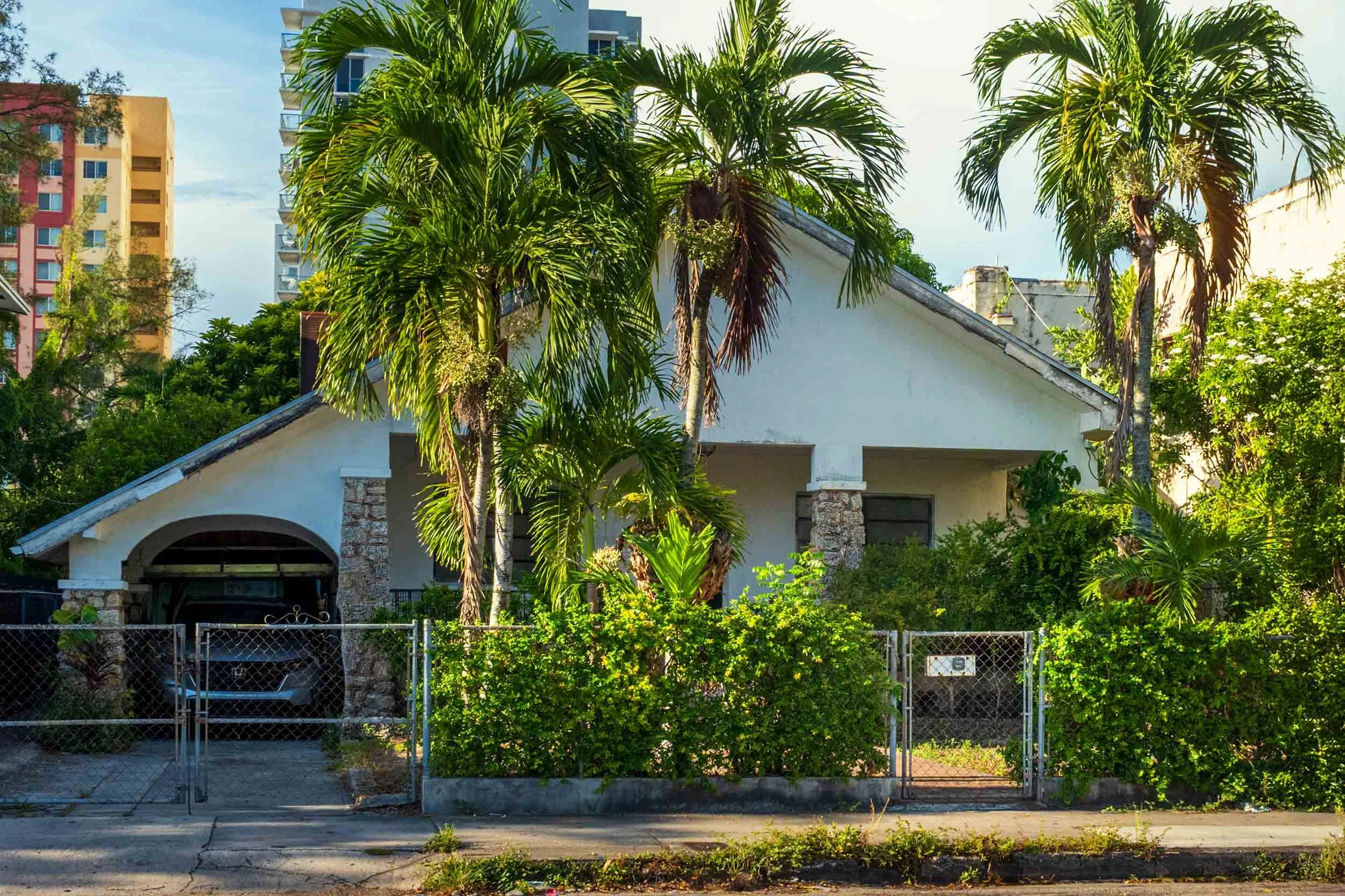 Blue Craftsman bungalow with stone porch columns, condo towers in the background, Miami
