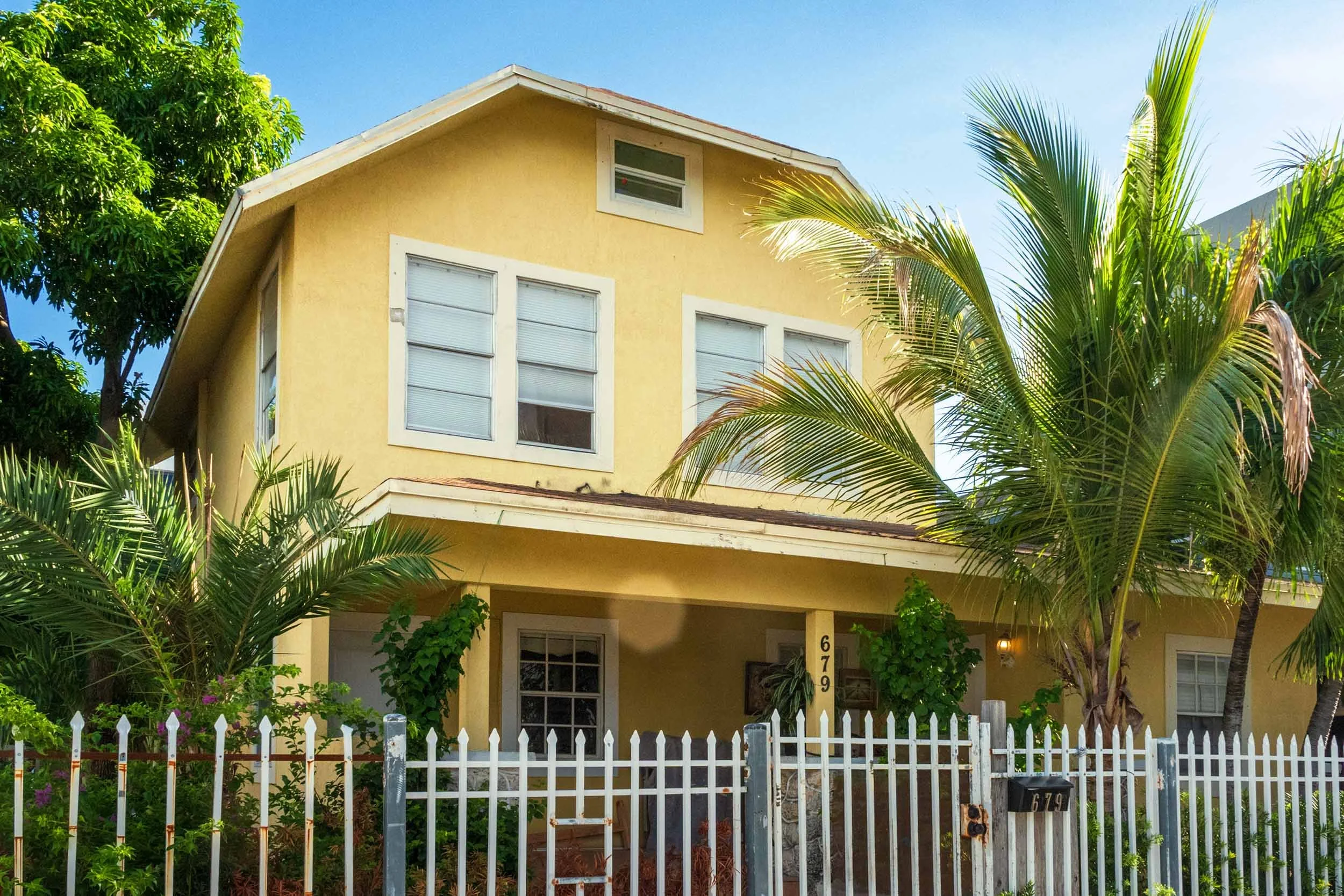 Yellow two-story house with a gambrel roof and palm trees, Miami