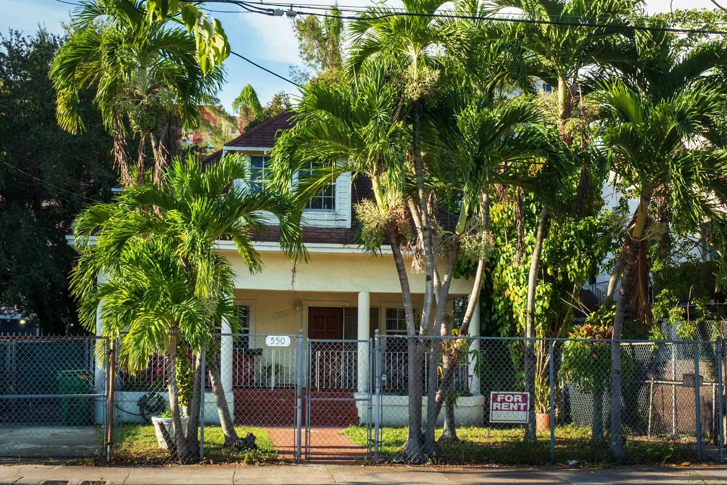 Yellow wood-frame house with a For Rent sign under palm trees, Miami
