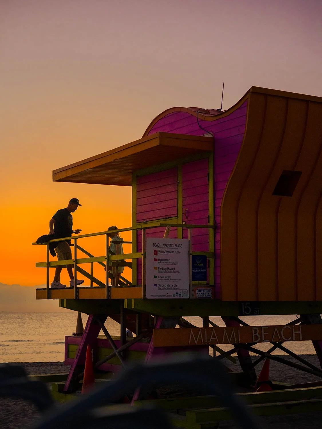 Father and child on a pink and orange Miami Beach lifeguard stand at sunset