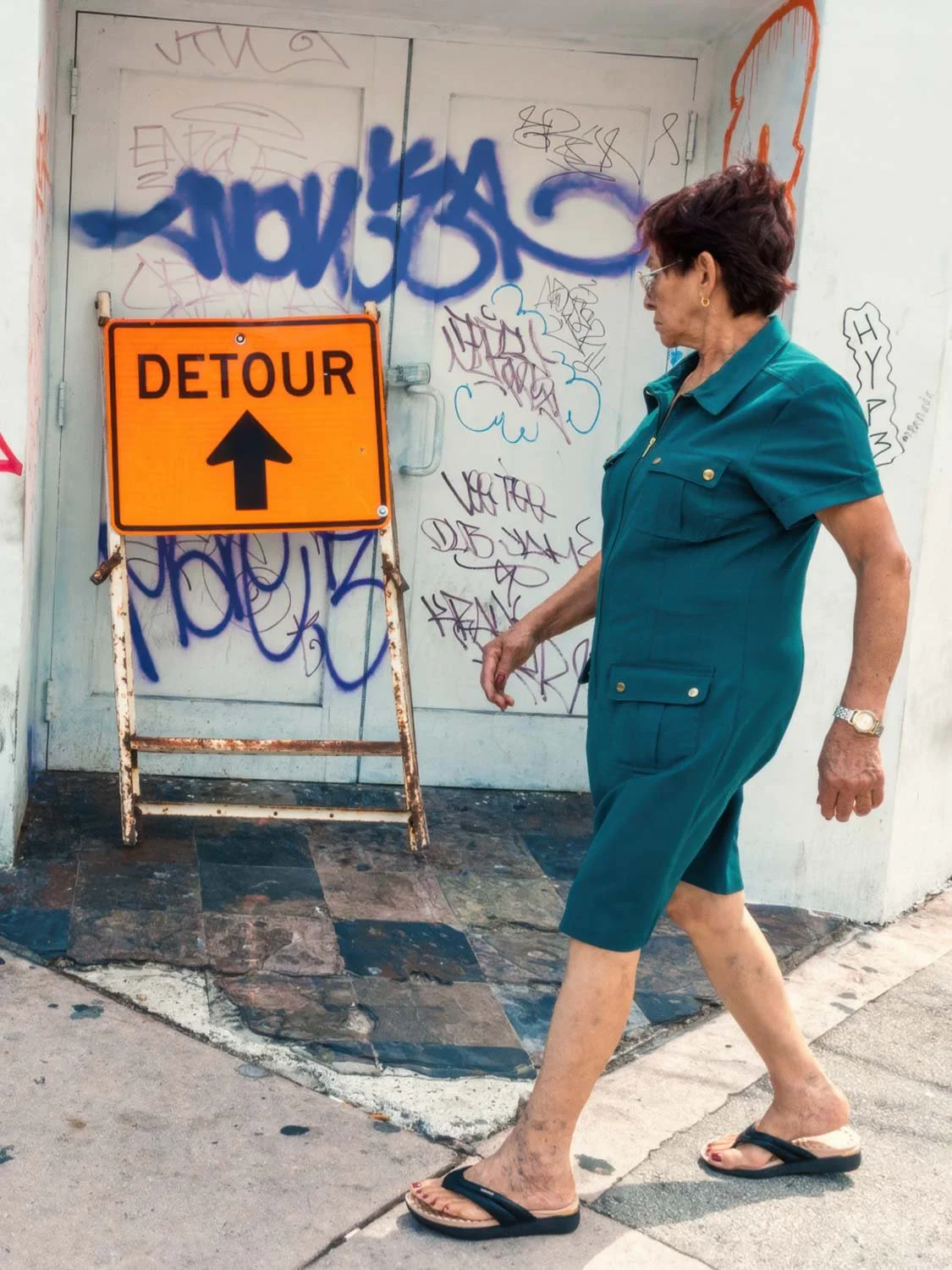 Older woman walking past orange detour sign and graffiti wall in Miami capturing candid urban street life