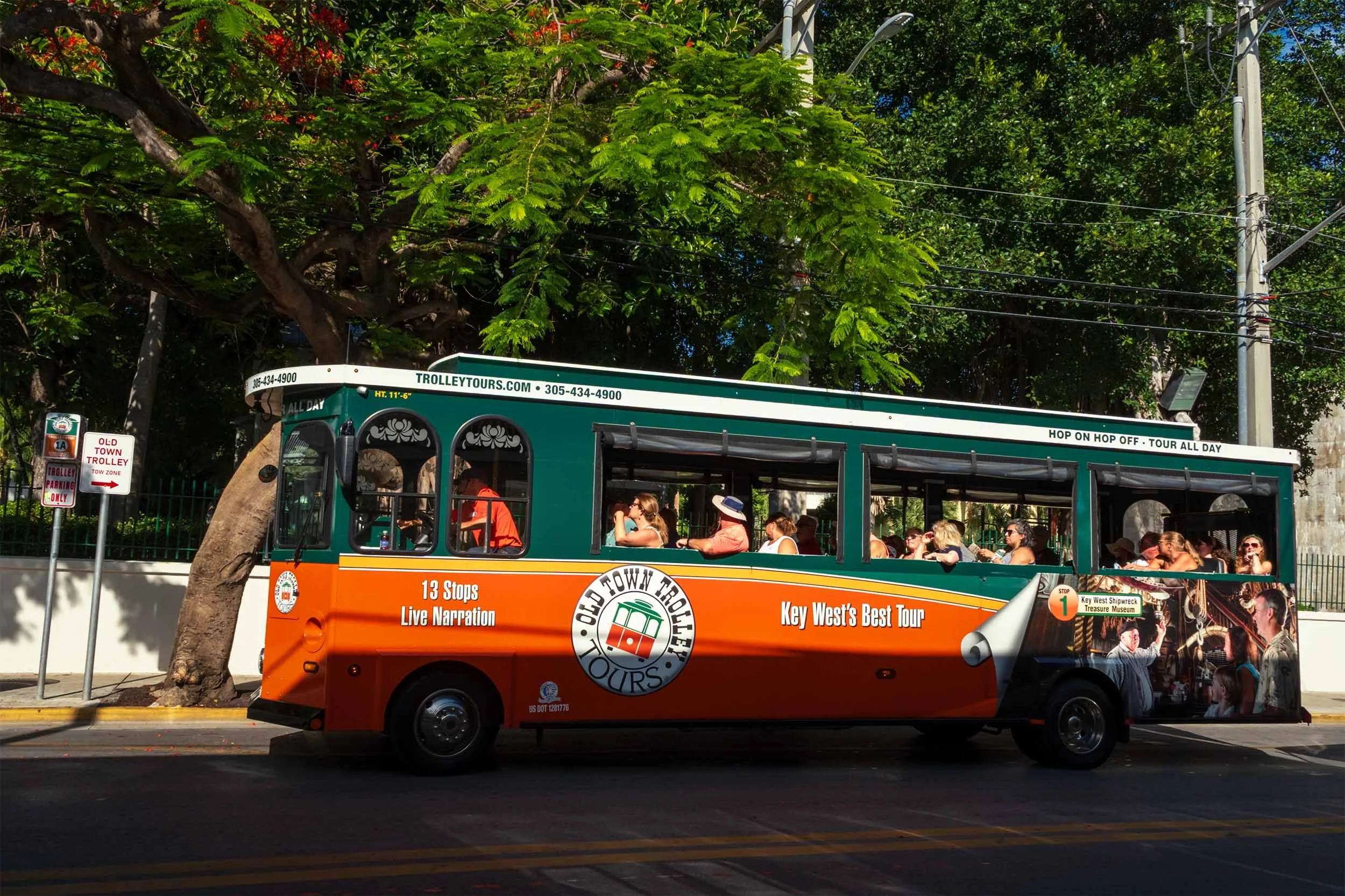Old Town Trolley Tours bus filled with passengers driving through a tree-lined street in Key West, Florida
