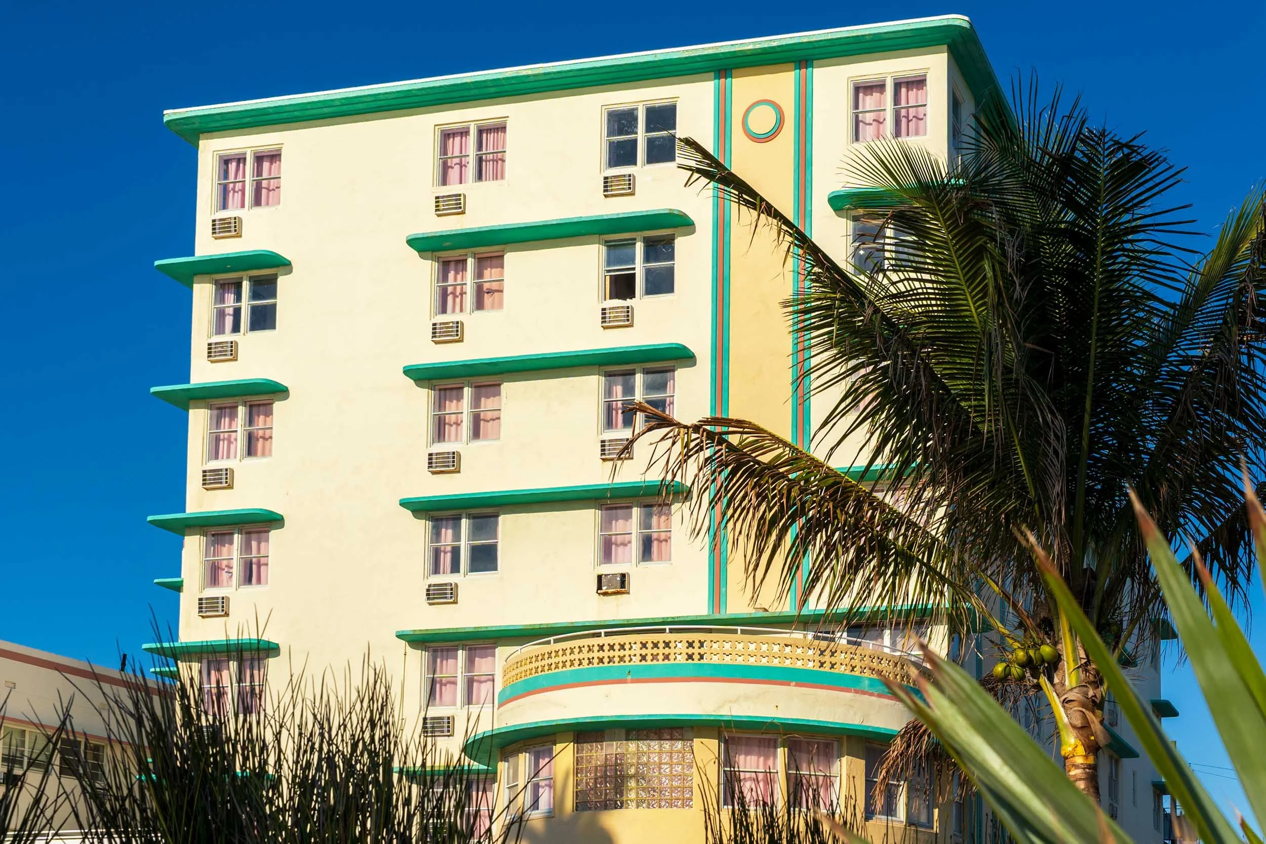The Broadmoor at 7450 Ocean Terrace showing green Deco banding and glass block, framed by palm trees