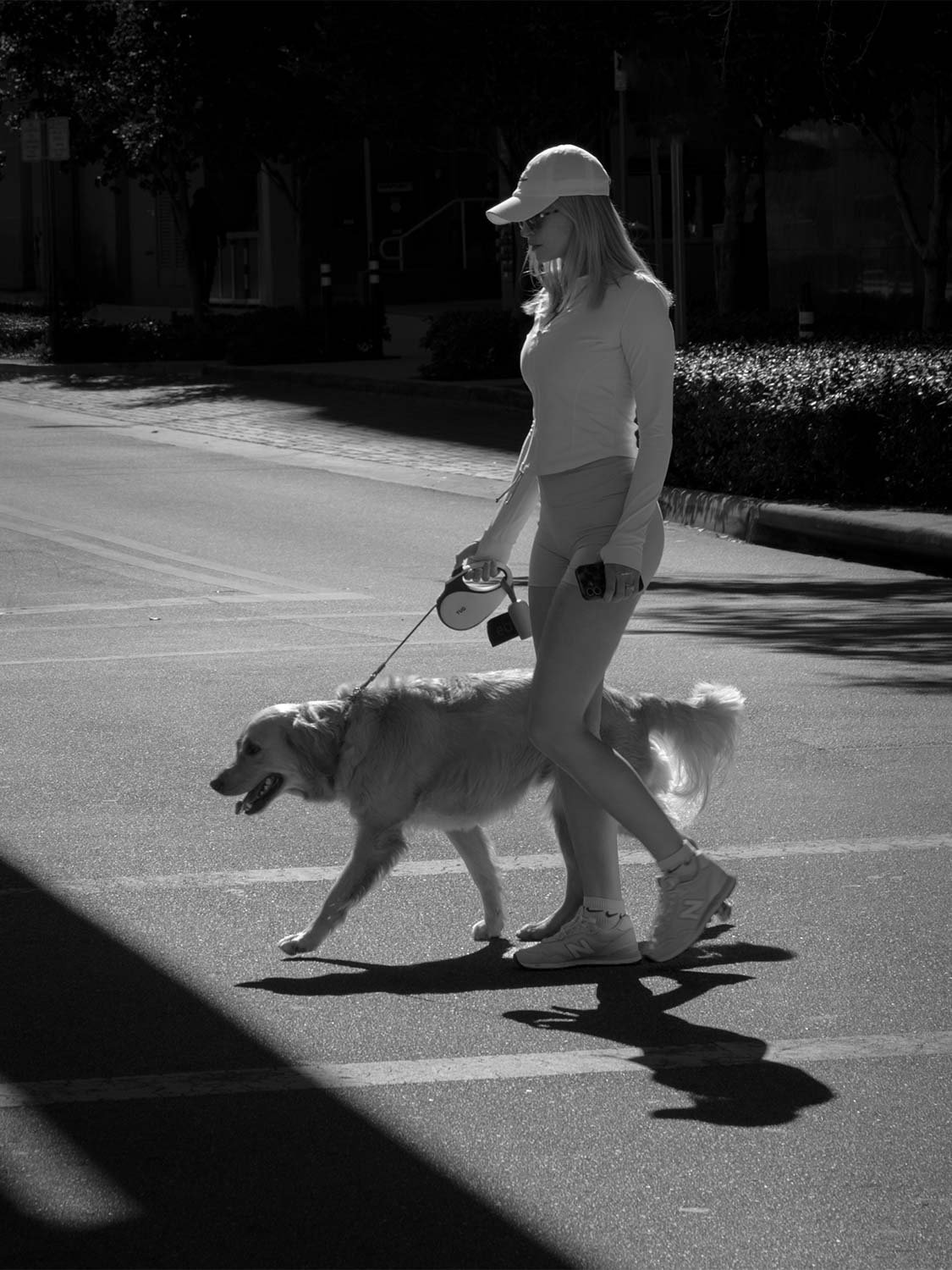 Woman walking golden retriever dog on leash urban street crosswalk athleisure outfit Nike sneakers lifestyle photo.