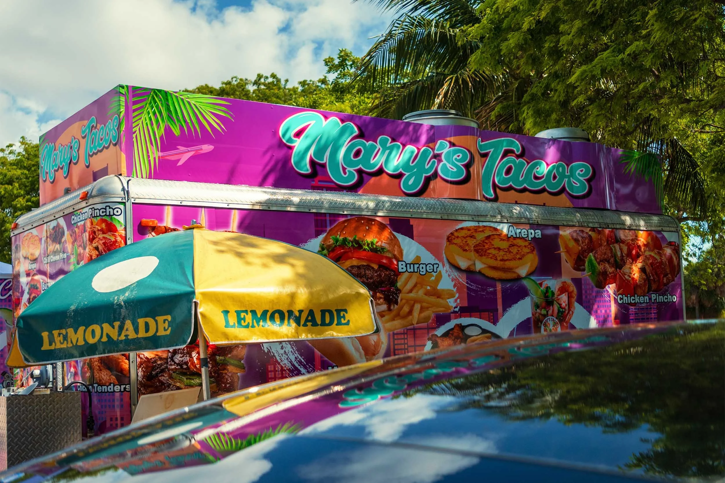 Mary's Tacos food truck at Hobie Beach Miami with lemonade umbrellas and a car reflection in the foreground