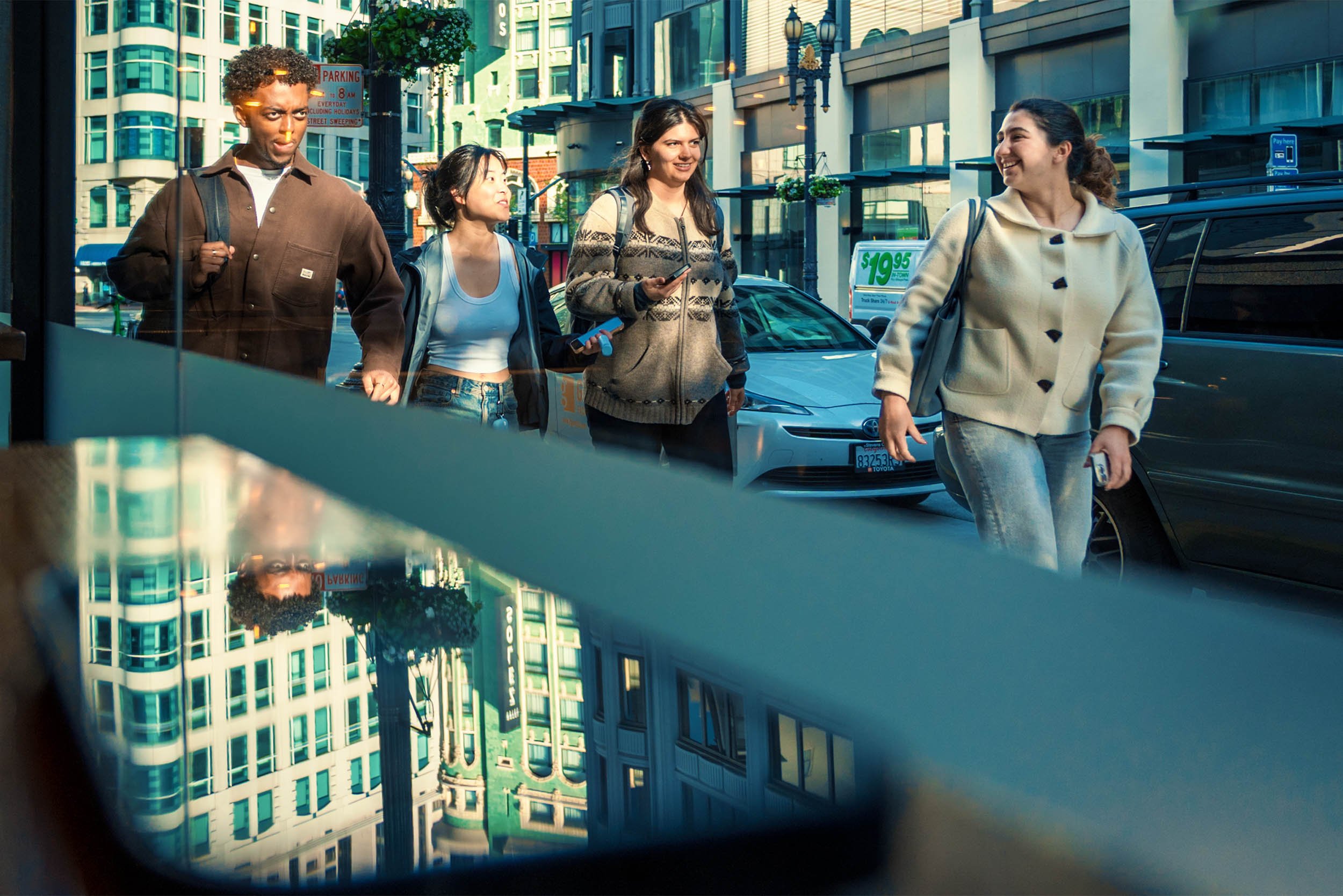 A group of young people are reflected in the window walking in downtown San 
Fransisco