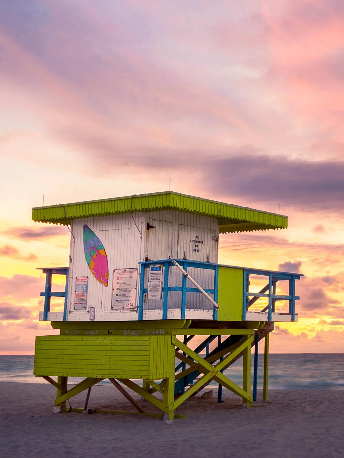Colorful Miami Beach lifeguard stand with lime green and blue trim at golden sunset, sandy shore and ocean backdrop