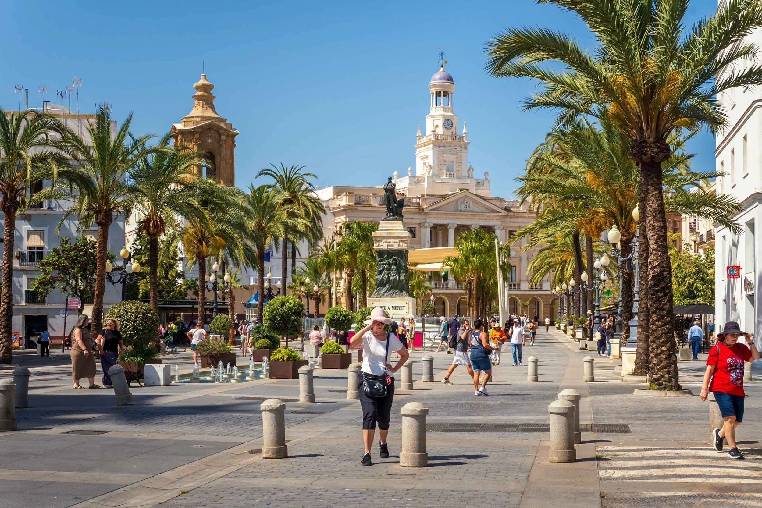 Tourists stroll Plaza de San Juan de Dios in Cadiz Spain with palm trees and neoclassical City Hall in background