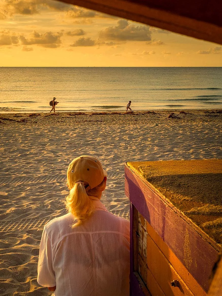Woman standing on the sandy shore of South Beach at golden hour, looking out toward the ocean