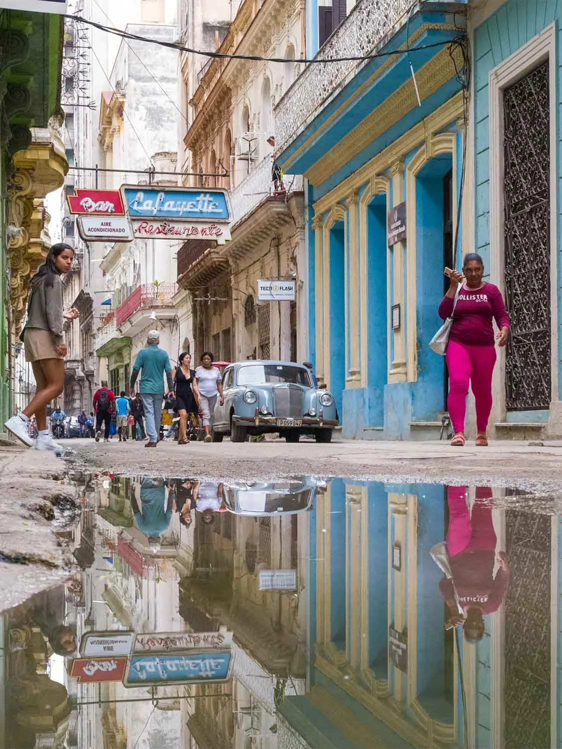 Old Havana Cuba street scene with classic car, puddle reflection, colonial architecture, and Lafayette Bar Restaurant sign.