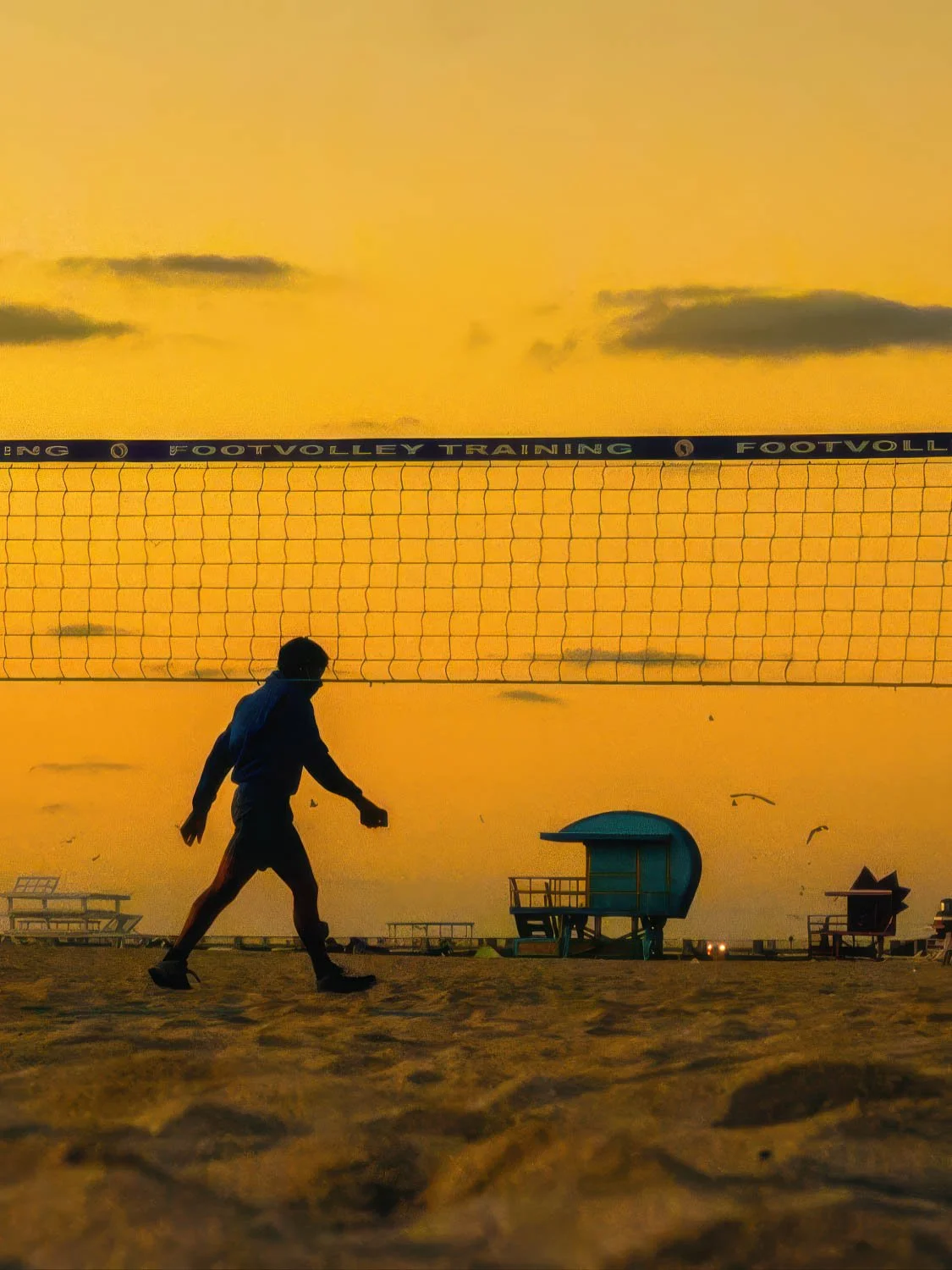Silhouette of a man playing footvolley on South Beach at sunrise with a golden orange sky