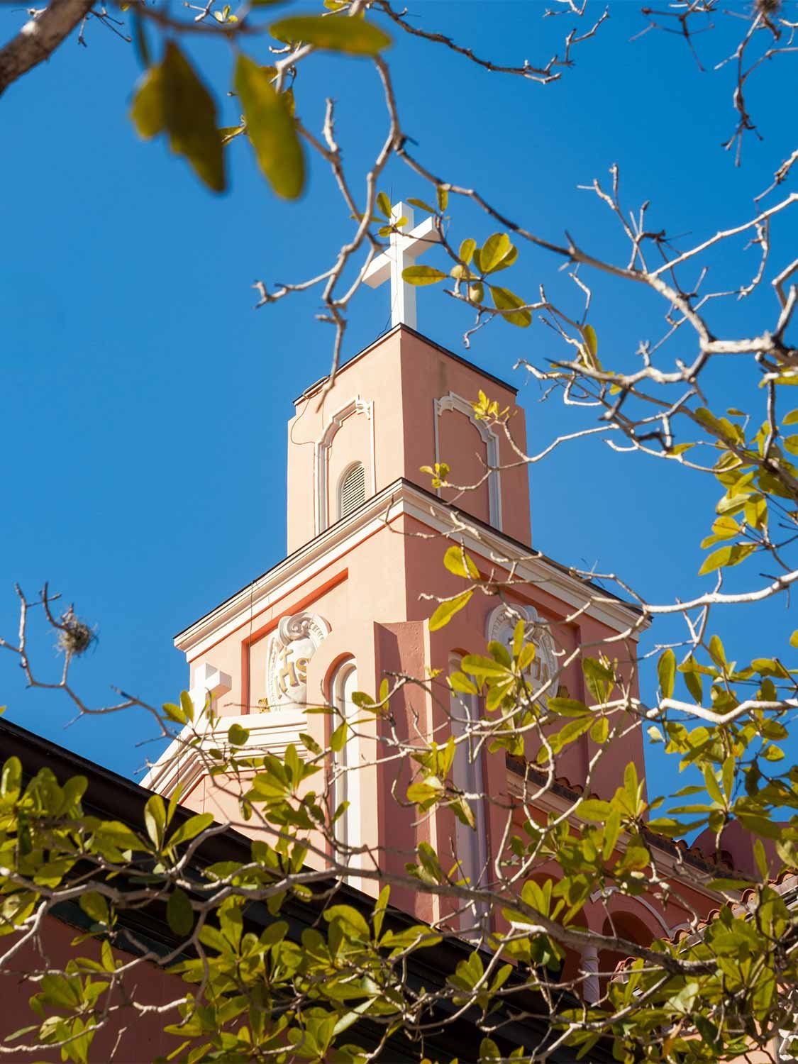 historic church steeple white cross pink facade religious landmark architecture blue sky tropical trees