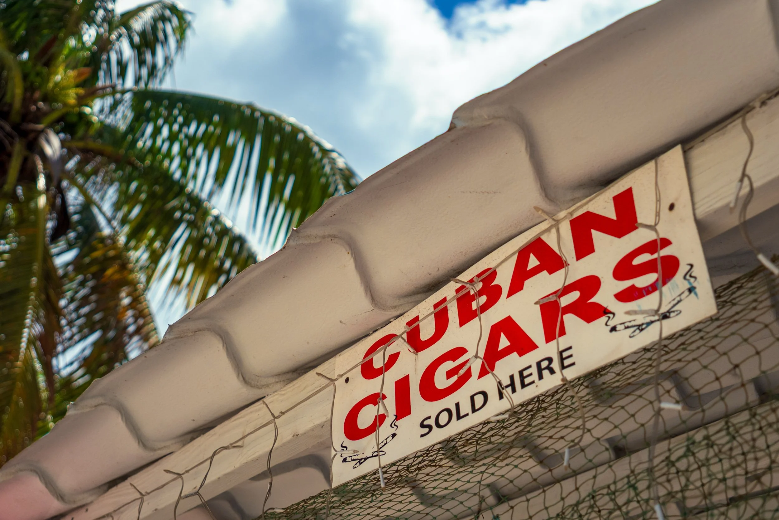 Cuban cigars sold here sign at Arawak Cay Nassau Bahamas, tropical cigar shop, red lettering on white board.