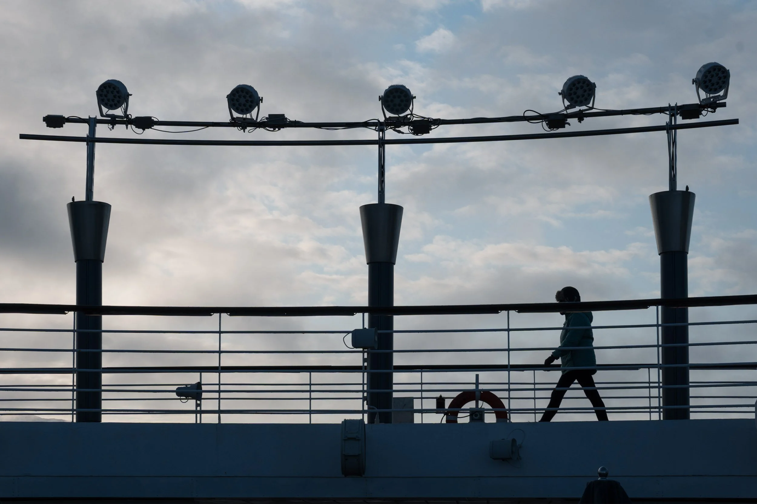 Deck light fixtures silhouetted against overcast sky, passenger walking below