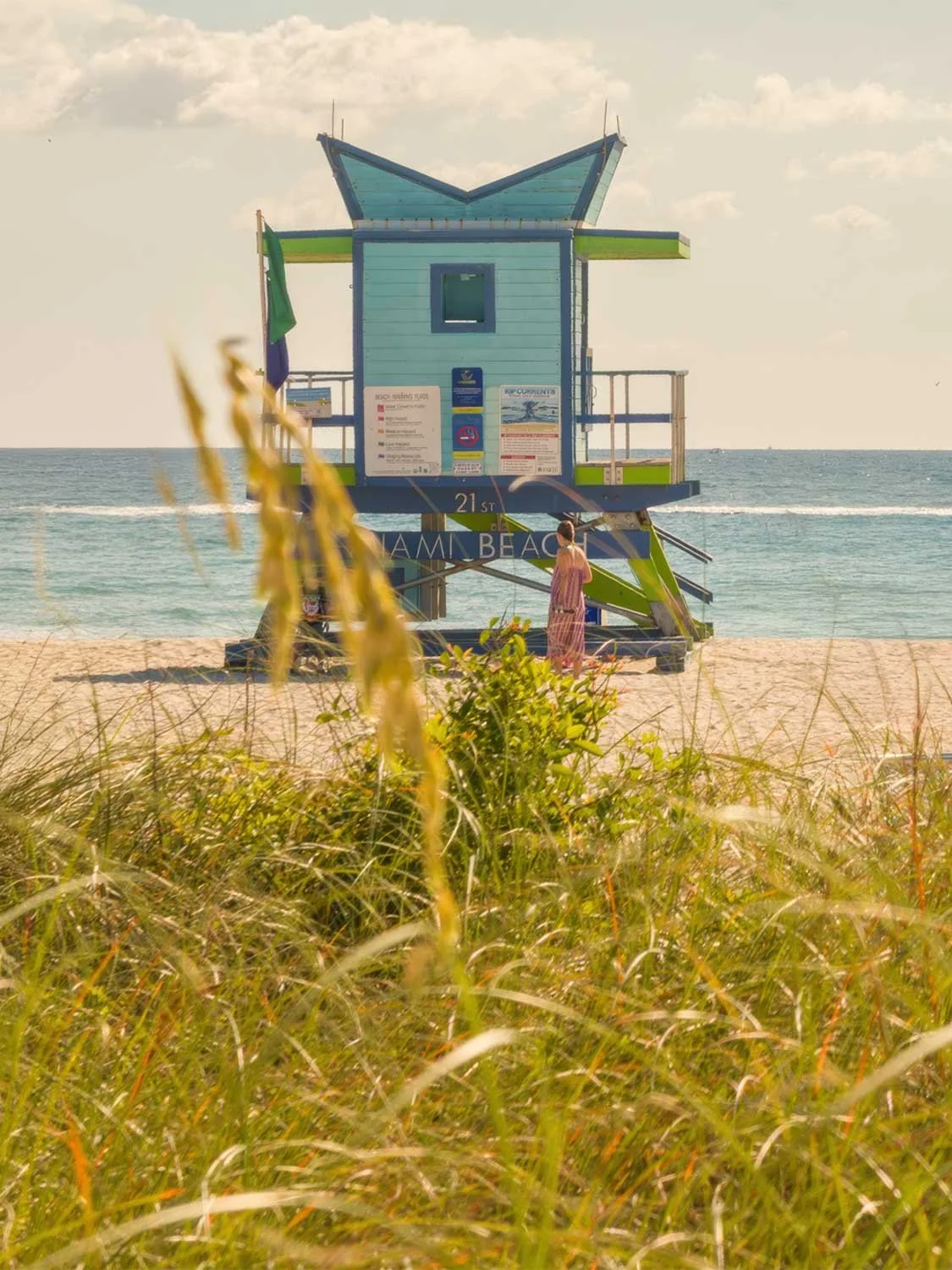 Blue and green Art Deco lifeguard stand at 21st Street on South Beach with a woman in a floral dress and ocean behind