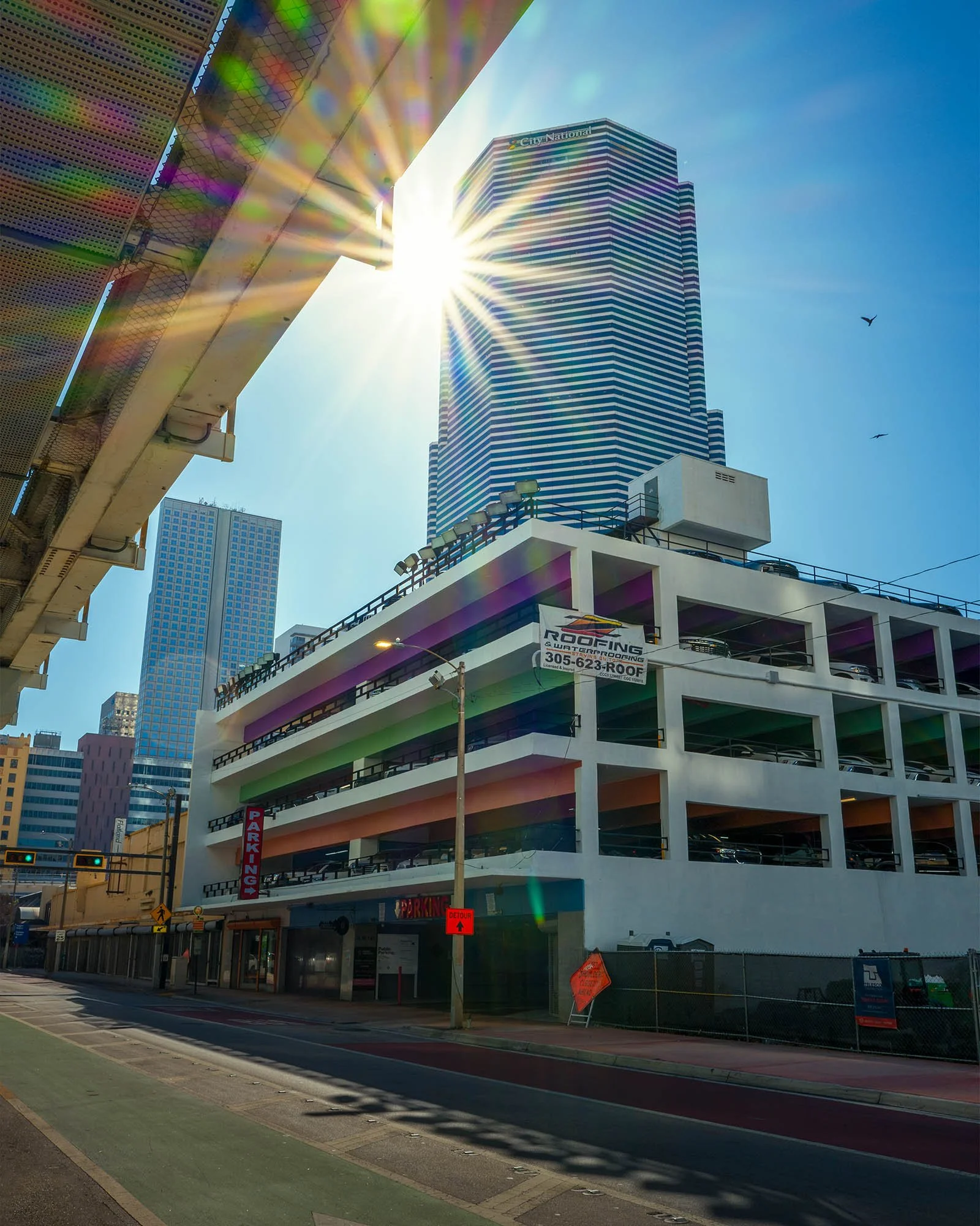 Sun flare with colored lens ghosting over a striped low-rise building and towers, Miami