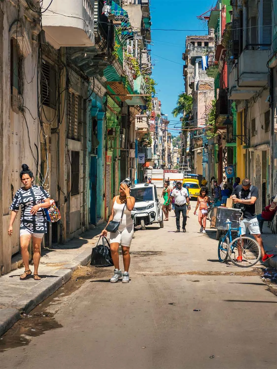 Old Havana Cuba street scene with locals walking past vibrant colonial architecture and vintage vehicles.