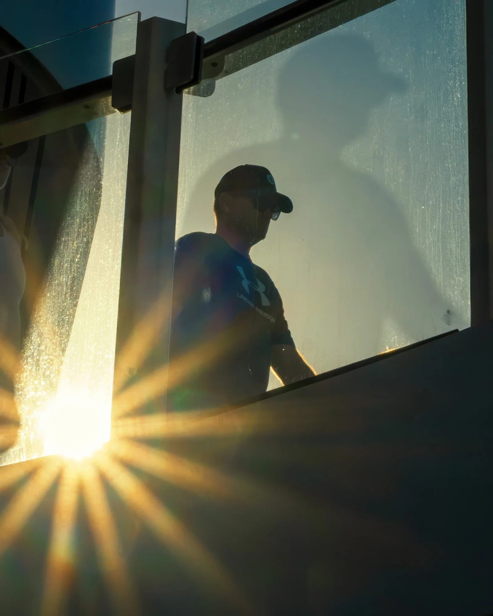 Man on a cruise ship running track behind a glass railing, sun flare bloated with too much sun showing