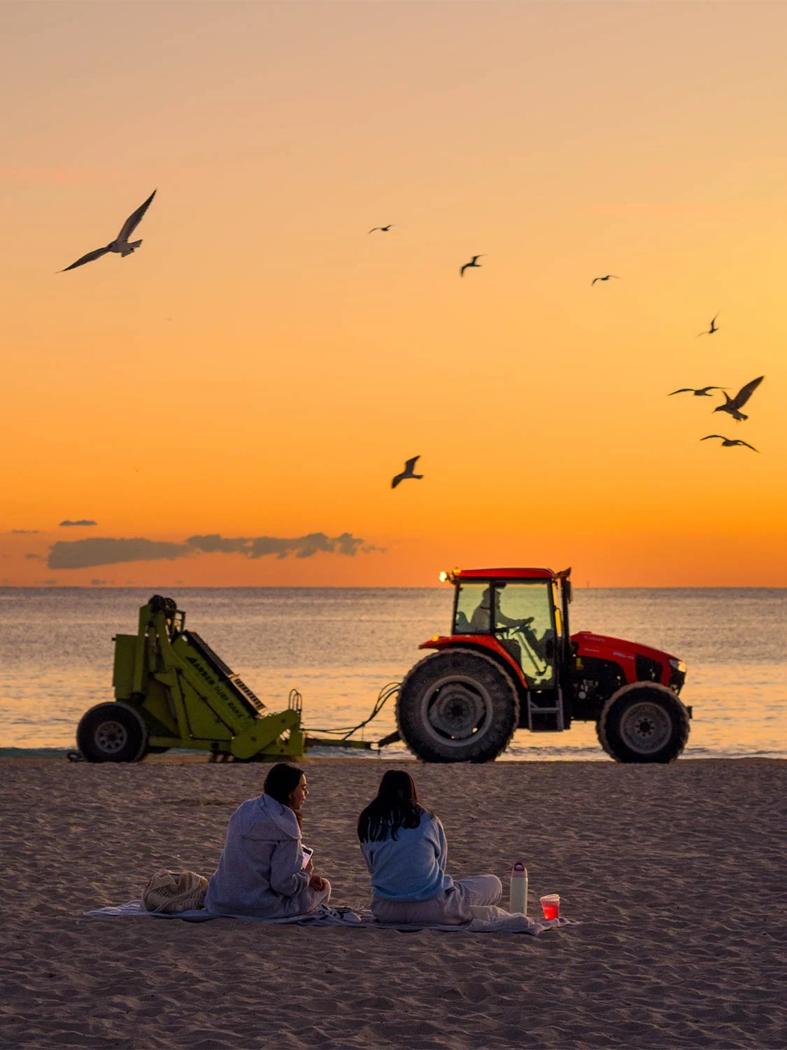 South Beach sunrise beach cleaning tractor seagulls golden sky two women sitting on sand Miami beach morning
