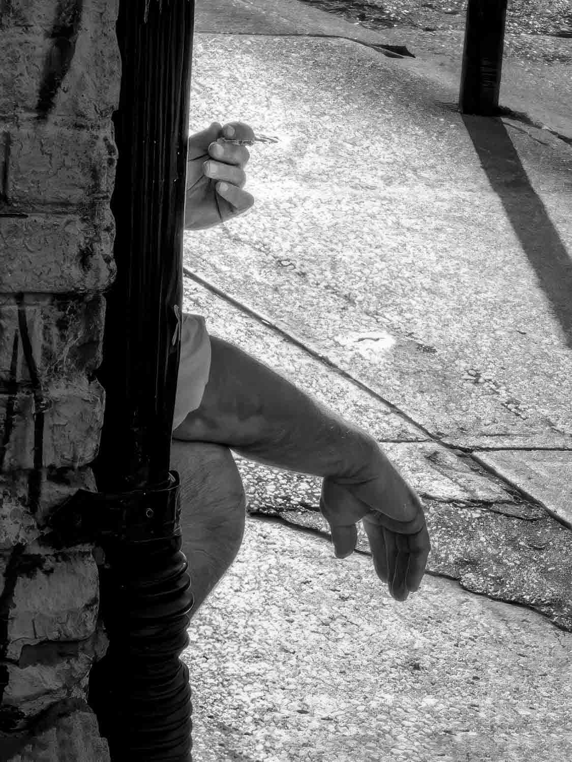 Hand holding keys on sidewalk Black and white close-up of a hand holding cigarette against a sunlit Miami sidewalk with dramatic shadows
