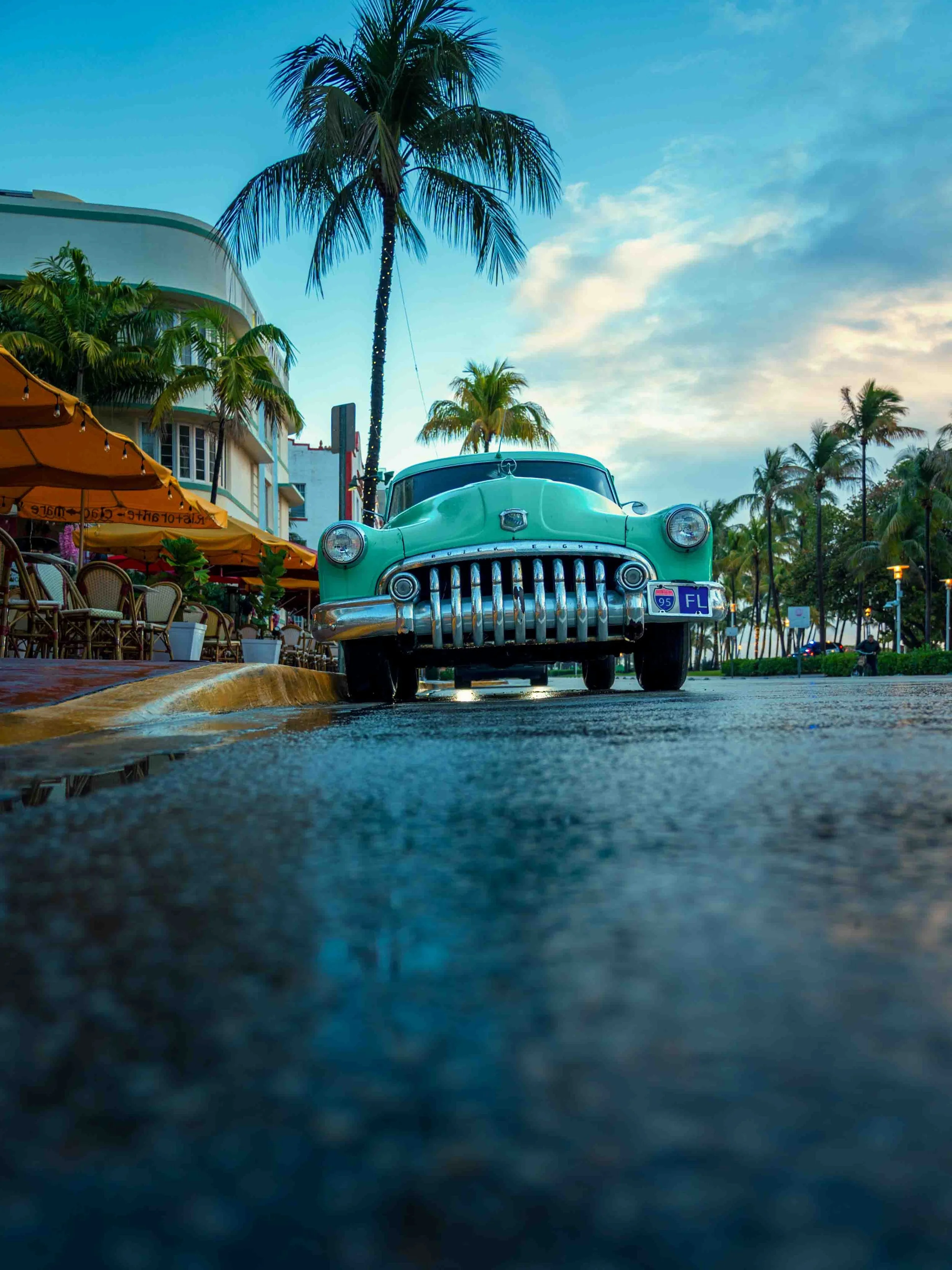Low-angle view of a mint green vintage Buick Eight parked on a wet Miami Beach street lined with palm trees