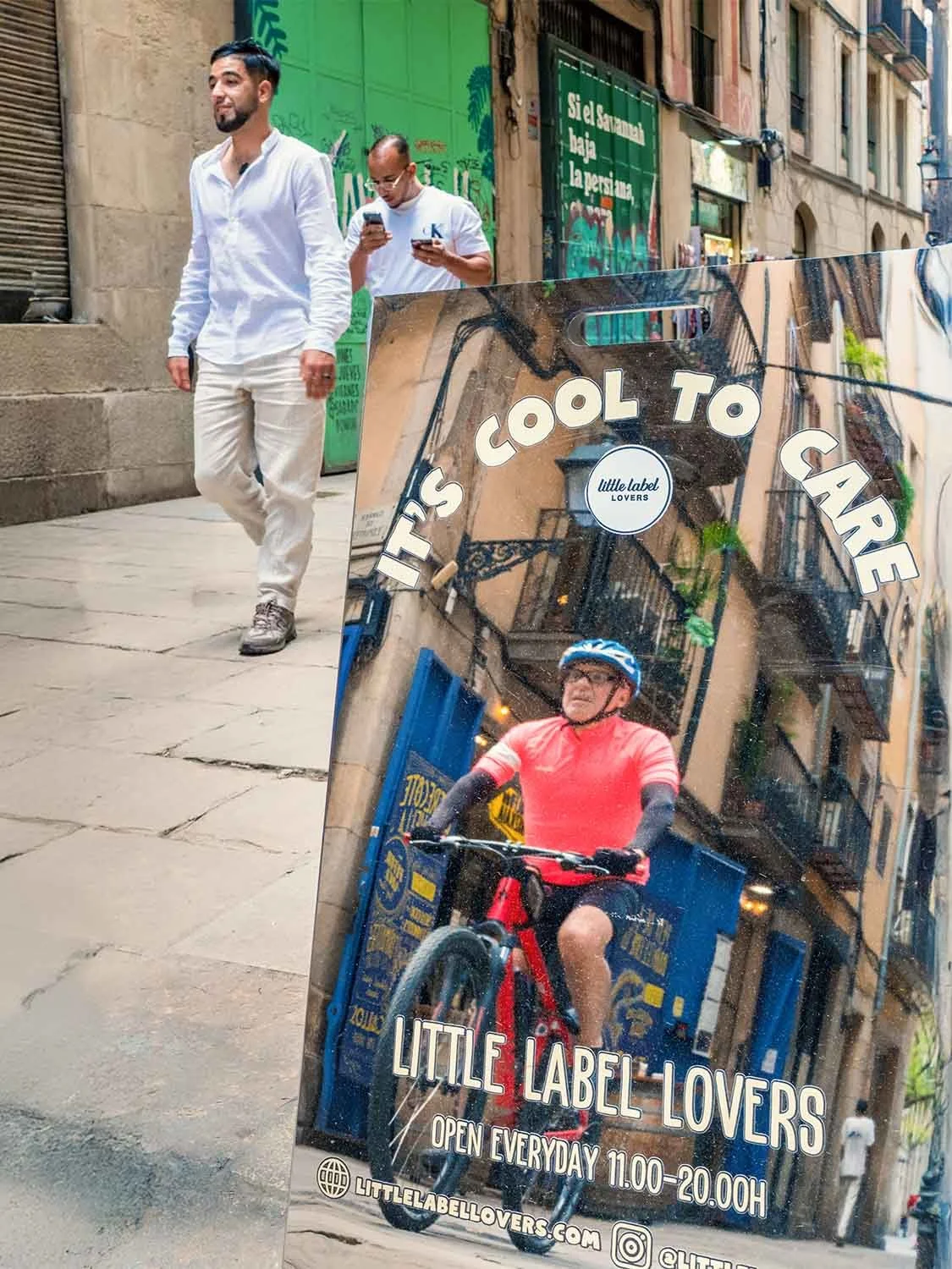 Men walking a narrow street in Barcelona behind a sidewalk sign showing a cyclist