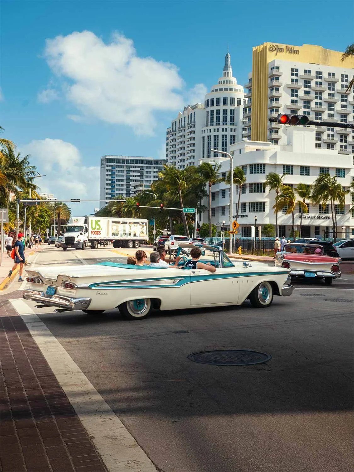 White and teal vintage convertible driving through Miami South Beach with Art Deco buildings and palm trees