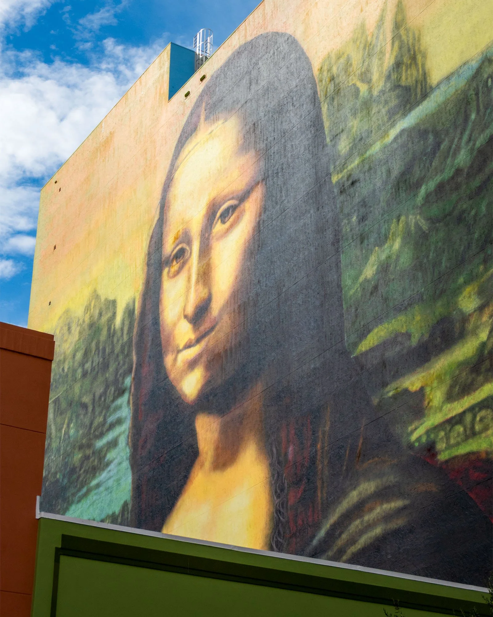 Mona Lisa mural at the top of a building, shot looking up against blue sky