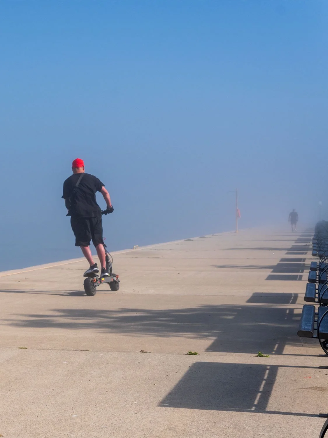 Electric scooter rider on waterfront boardwalk | urban micro-mobility | foggy seaside promenade outdoor lifestyle