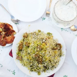 Baghali Polo with lamb, served with sides of potato tadig and yogurt with cucumber and mint.