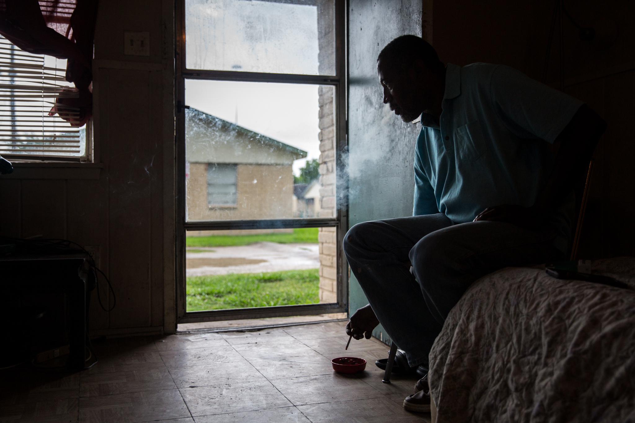 George James Jr., 51, smokes a cigarette in his living room that also serves as his current bedroom at his home in Houston. James, who is legally blind and on disability, feels left behind waiting for assistance to help repair his storm-damaged home.