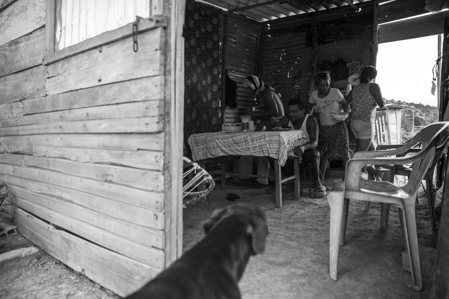  Lisandro Sanchez and his family prepare to eat lunch while their dog wiats for scraps by the door.  Families in Alfonso Gomez subsist off beans, rice, peas with occasional meats like hot dogs. Families go to the Cucuta’s wholesale market, when trans