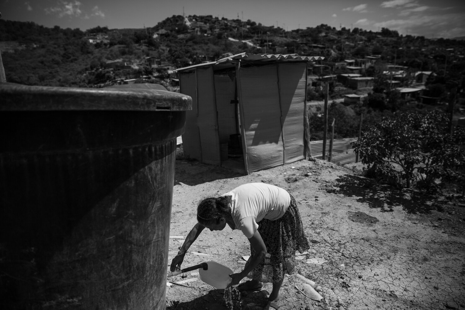  Yenis Davila fills a container with drinking water from a storage tank in the backyard. Some families have received donated water tanks from charity organizations. Others keep multiple buckets of water filled to the top at all times – split between 