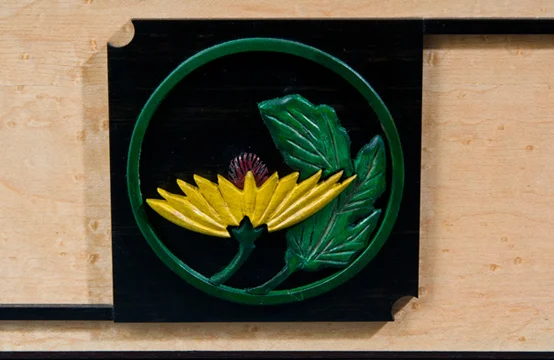 Close-up of a decorative metal artwork featuring a yellow flower, green leaves, and a green dome, mounted on a black background.